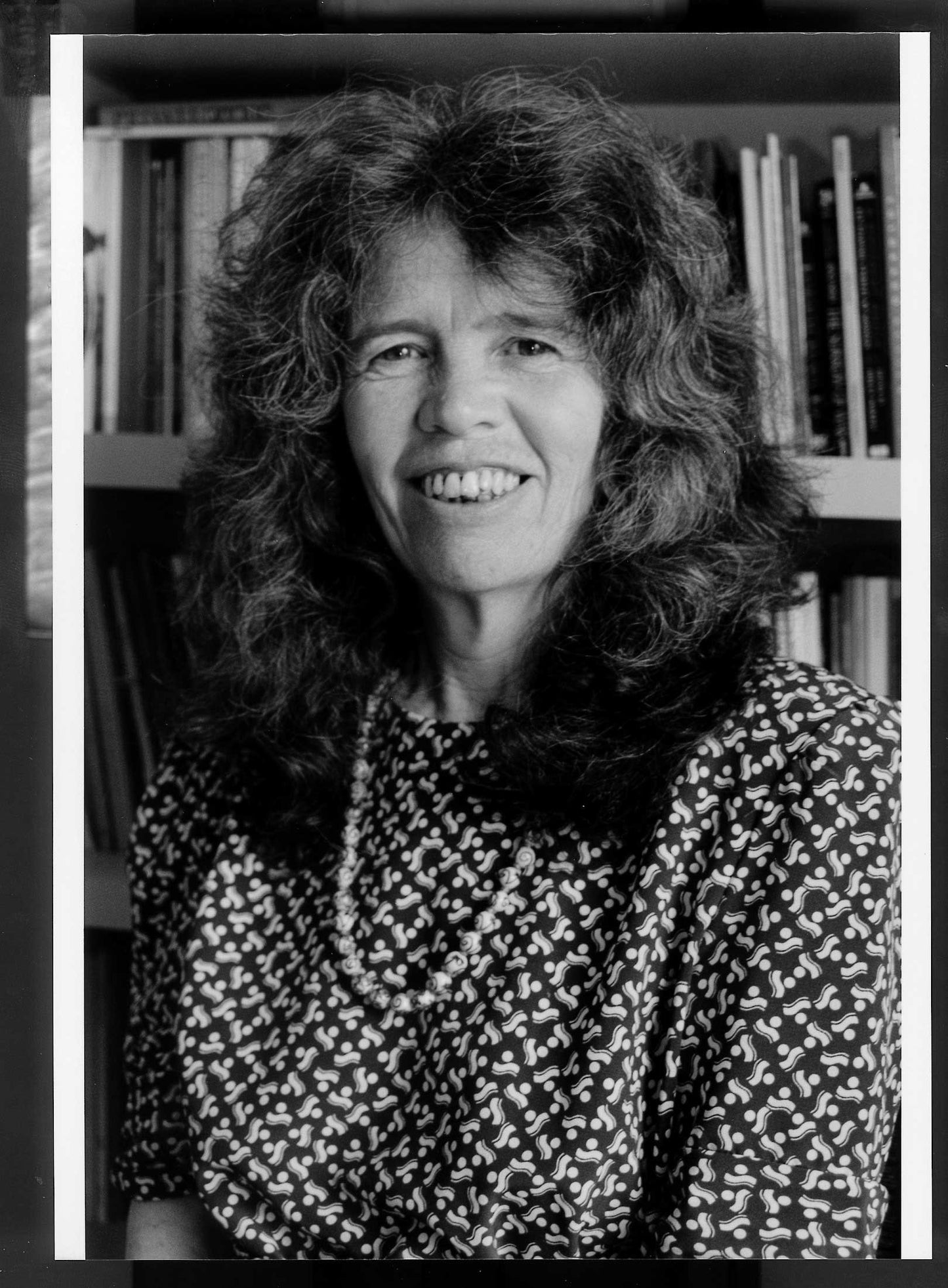 Black and white photo of a woman with shoulder-length hair in front of bookshelves.